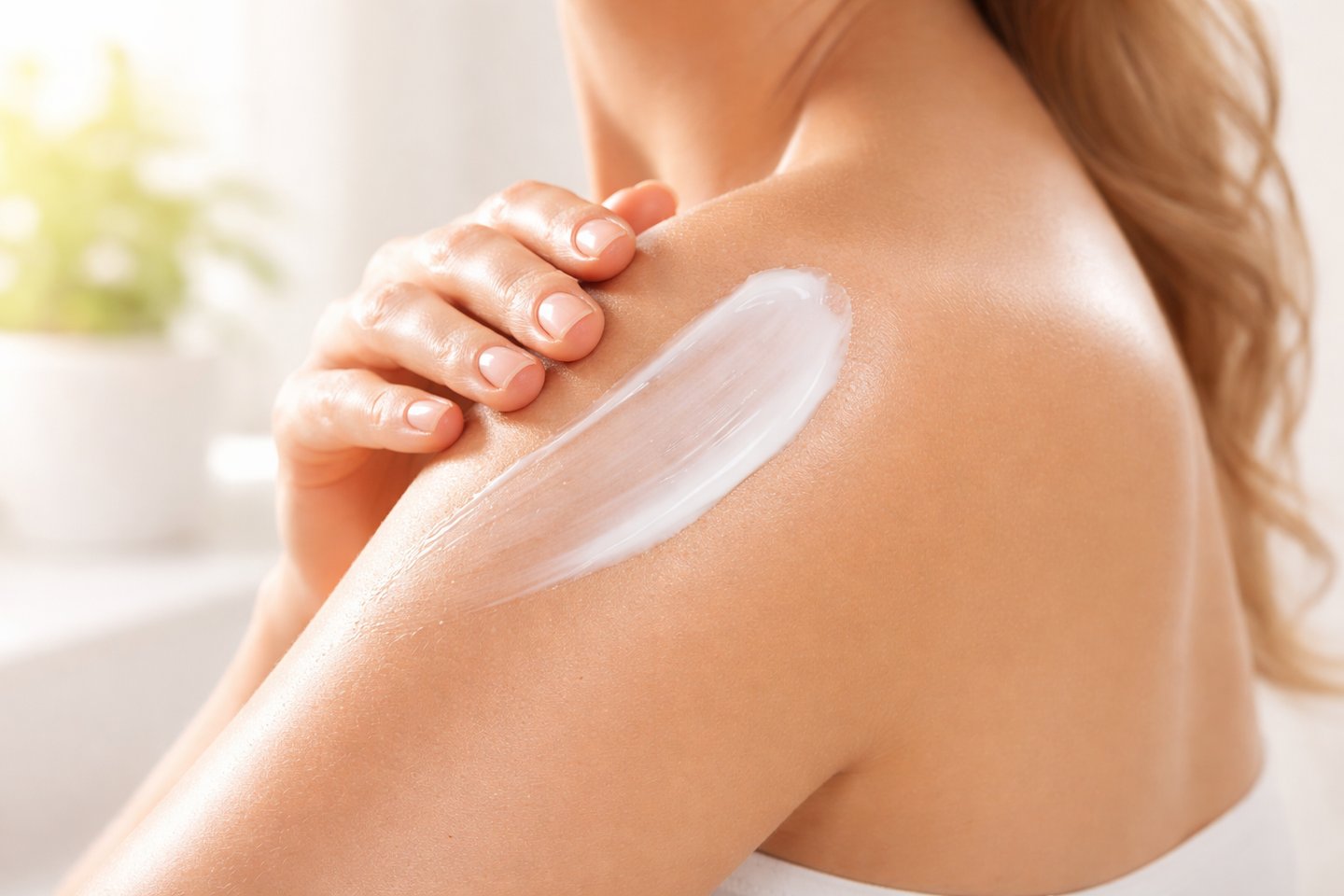 Woman applying white moisturizing body lotion to her shoulder for hydrated skin.