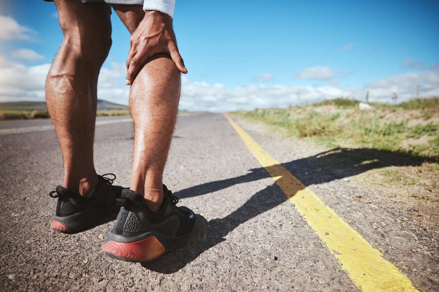 A runner holds his calf muscle in pain while standing on a road, representing a sports injury.