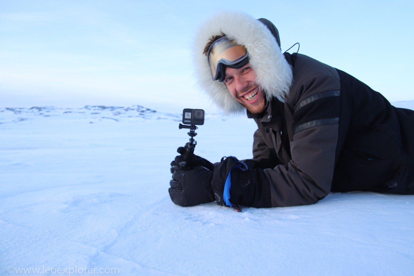 Un explorateur souriant, vêtu d'une parka en fourrure, filme un paysage arctique sur la neige