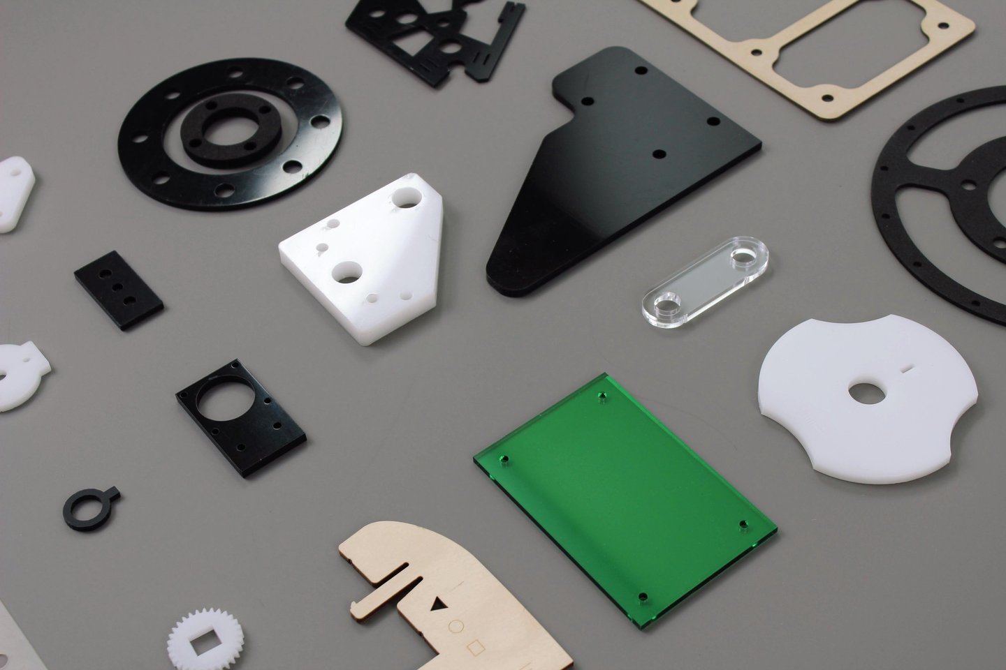 Collection of precision laser cut plastic, acrylic, and wood industrial components on a gray surface.