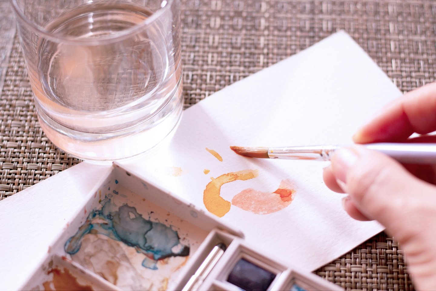 Artist painting orange watercolor strokes on paper with a brush and water glass.