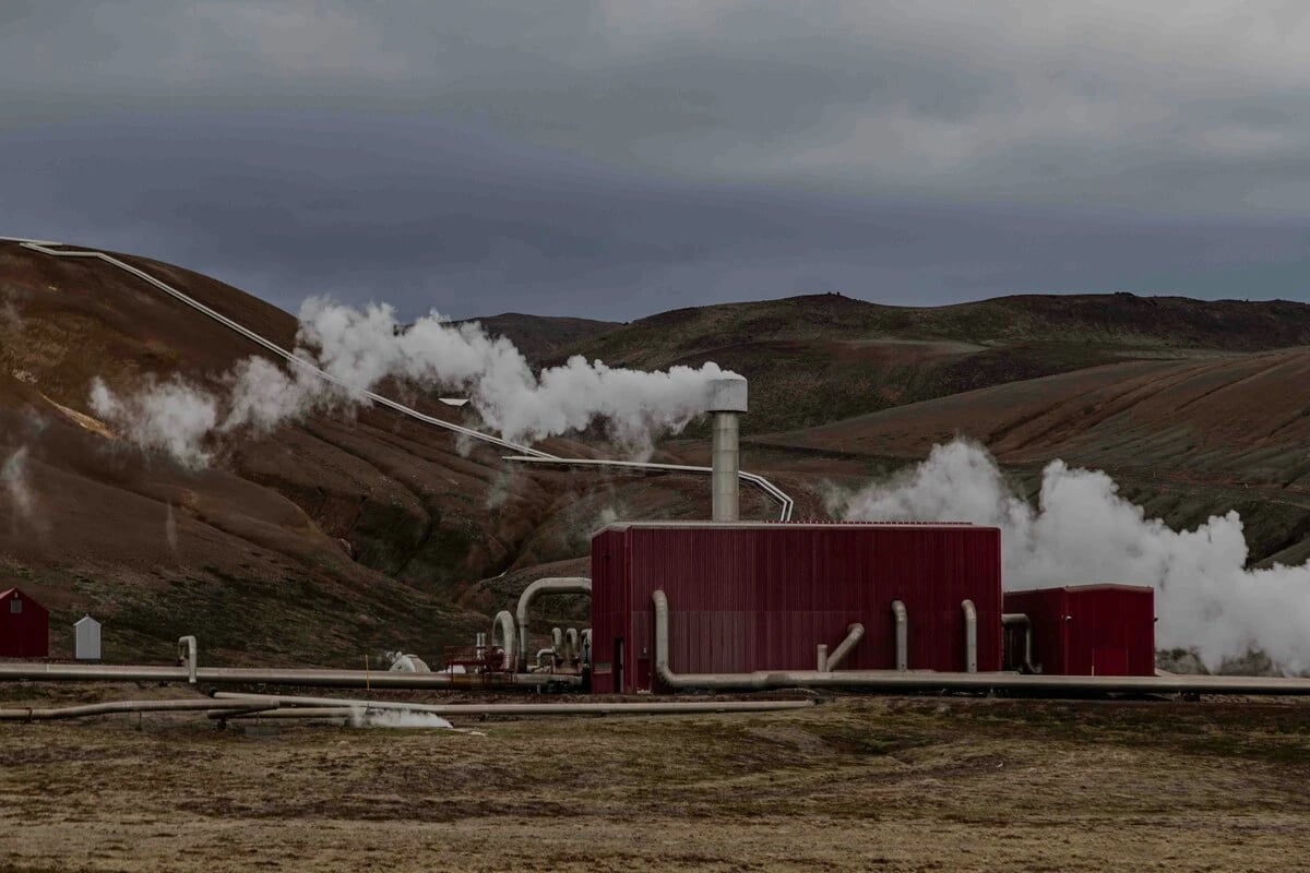 Geothermal power plant in Iceland emitting steam from a red building amidst rugged volcanic hills.