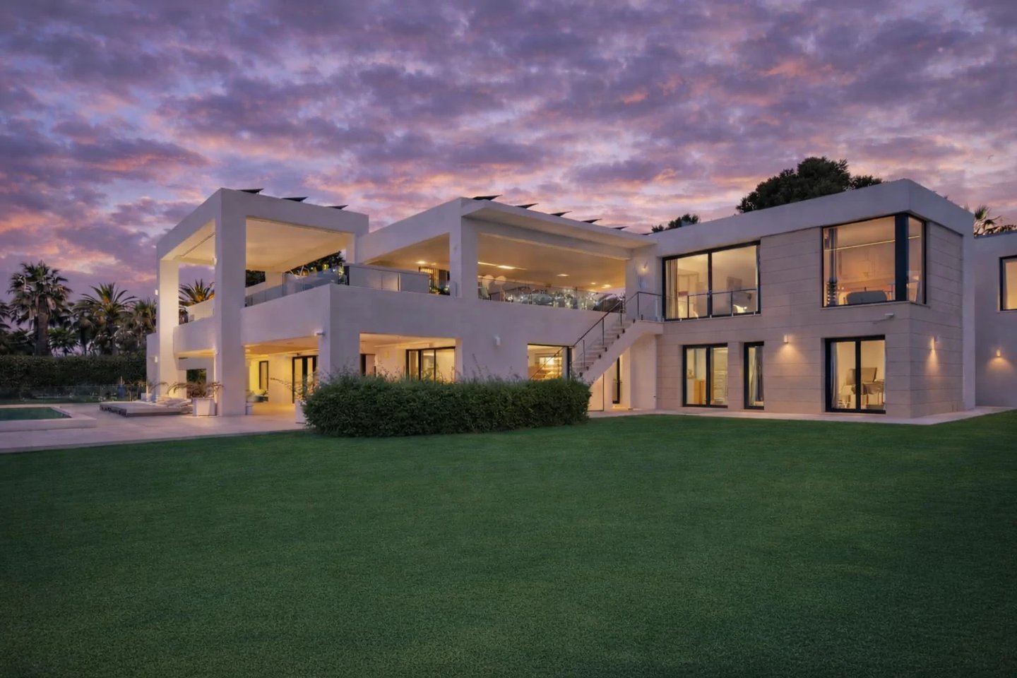 Modern beachfront villa at dusk with illuminated interiors and dramatic clouded sky