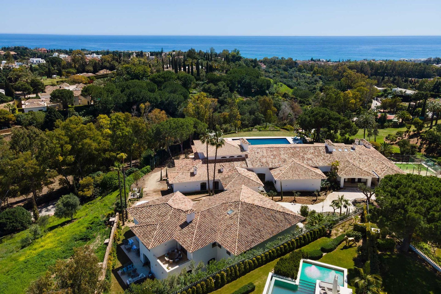 Aerial view of estate with pool, tennis court and sea backdrop
