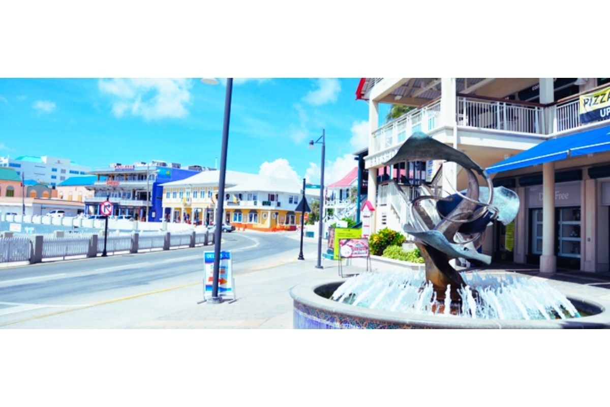 Rua de lojas e galerias em George Town, Ilhas Cayman, com fachadas coloridas e movimento de turistas.