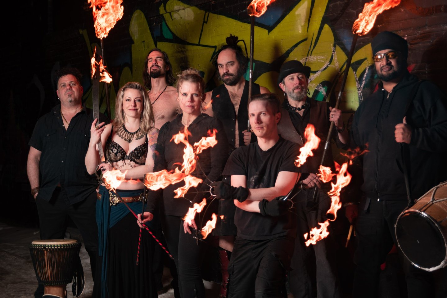 Flame Syndicate fire and music team pose in front of a wall full of graffiti art