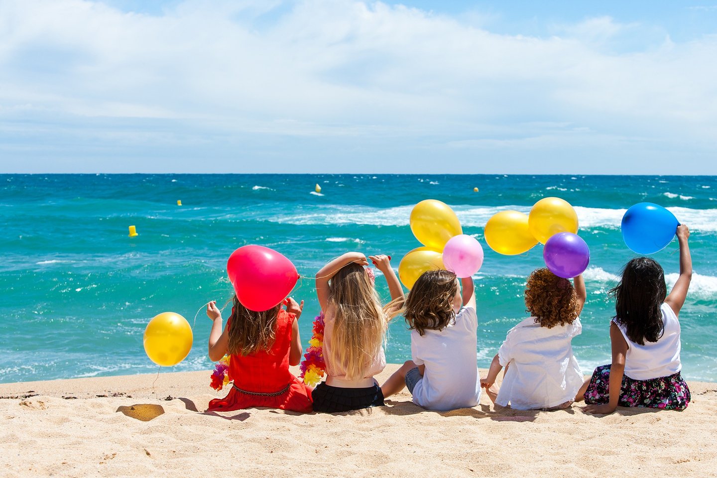 Children sitting on beach with color balloons