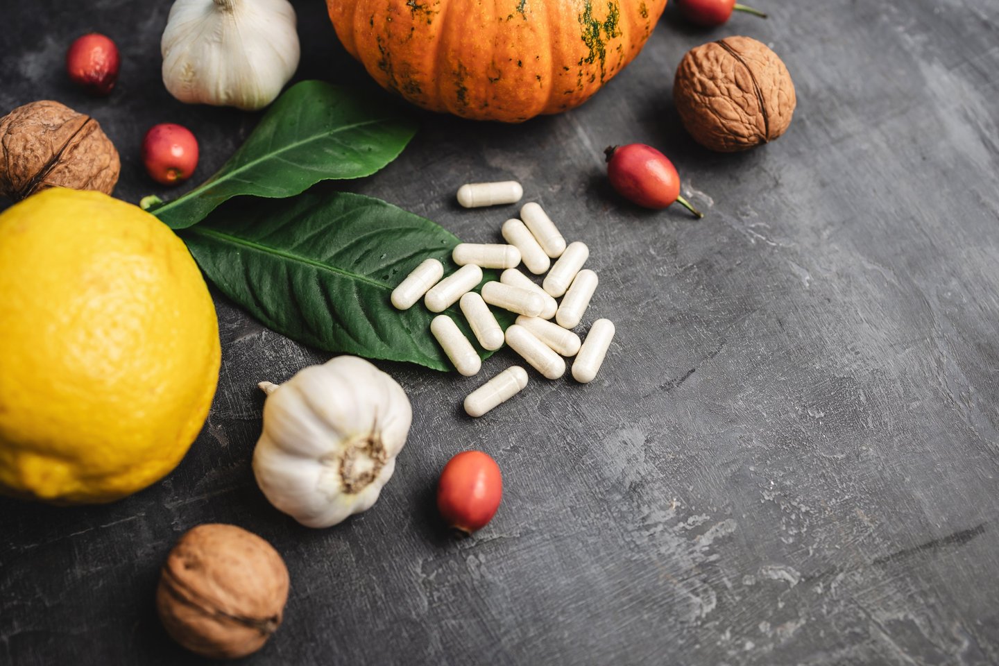supplement pills, head of garlic, spinach leaf, lemon, and other fruits and vegetables on a table