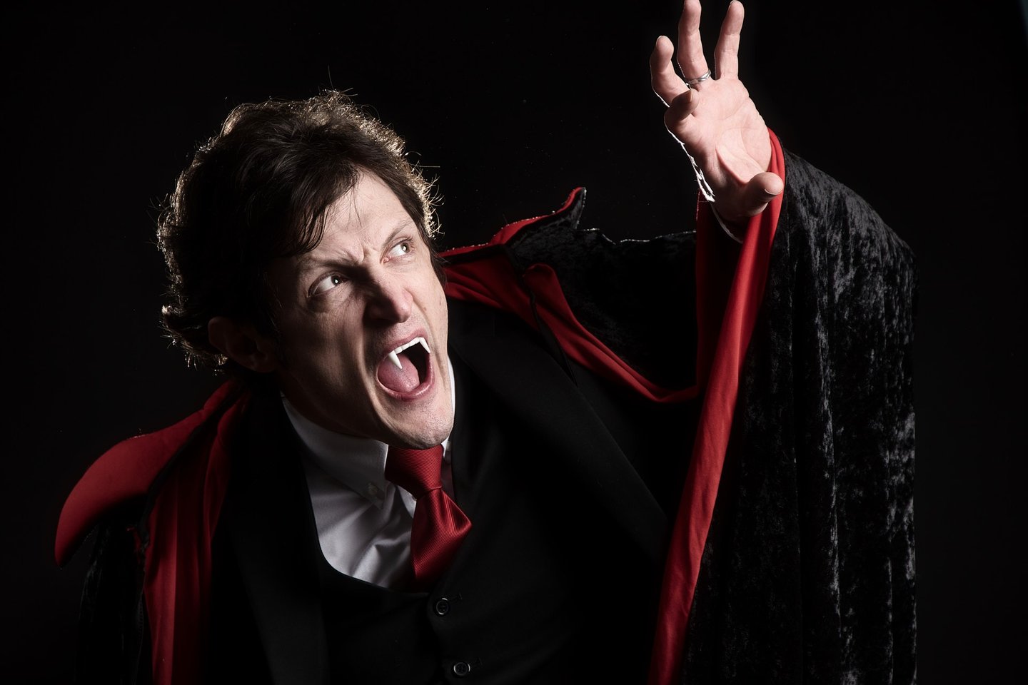 a man in a dracula costume with a red capelet looking like a vampire being scared of the sunlight