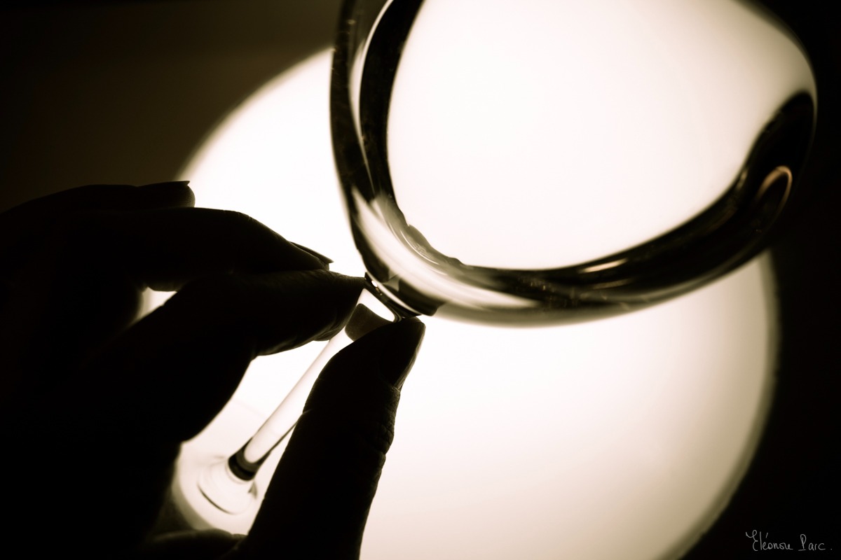 Vue en gros plan d’un verre de vin de profil, avec des doigt qui tiennent le pied du verre.