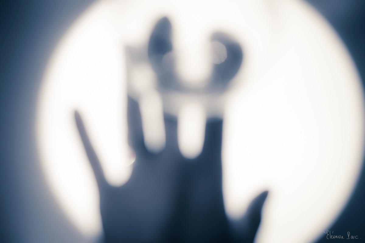 Vin Fantomatique – Silhouette de main devant un cercle de lumière, verrerie floue, vin