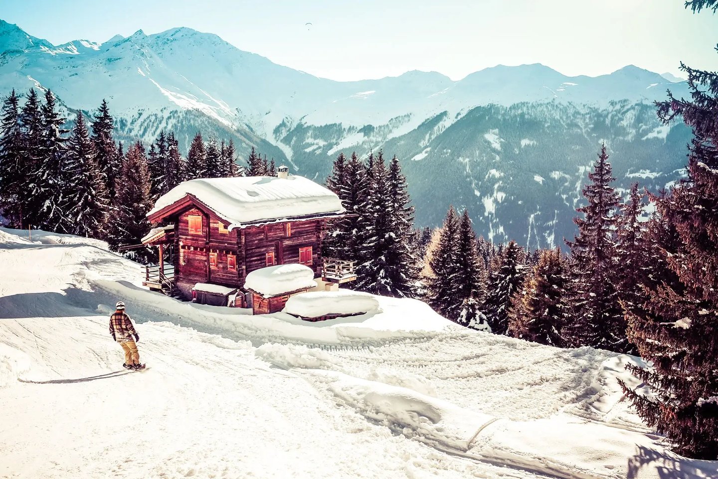 Verbier in winter, with a snow covered lodge, skier, pine trees and snow capped mountains.
