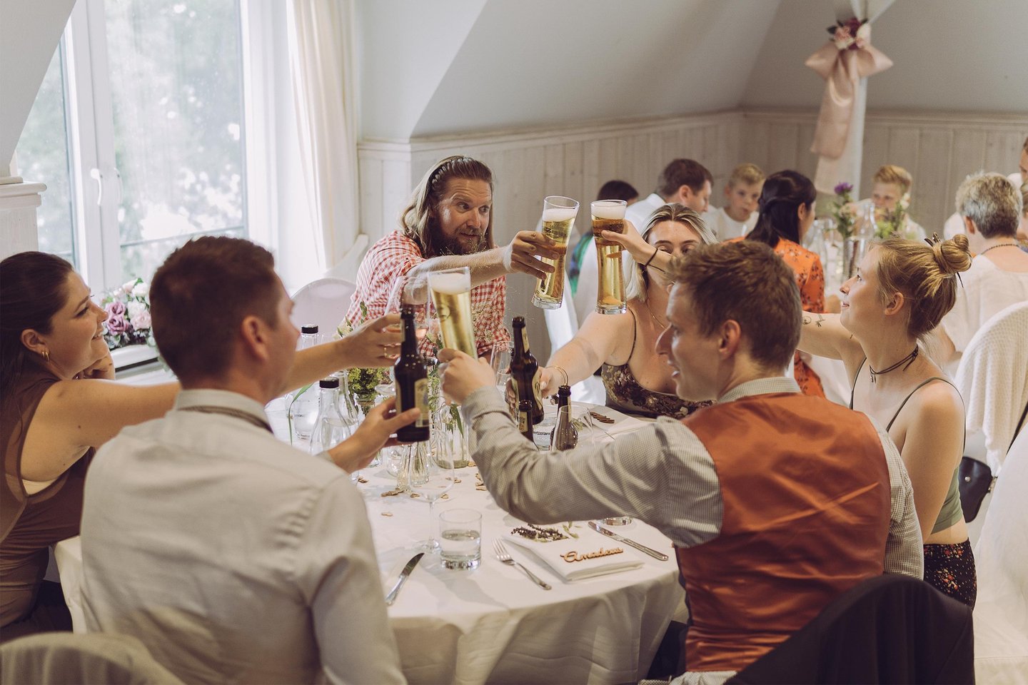 Hochzeitsgäste stoßen fröhlich mit Biergläsern am Tisch an. Authentische Eventfotografie von Just Perspectives.