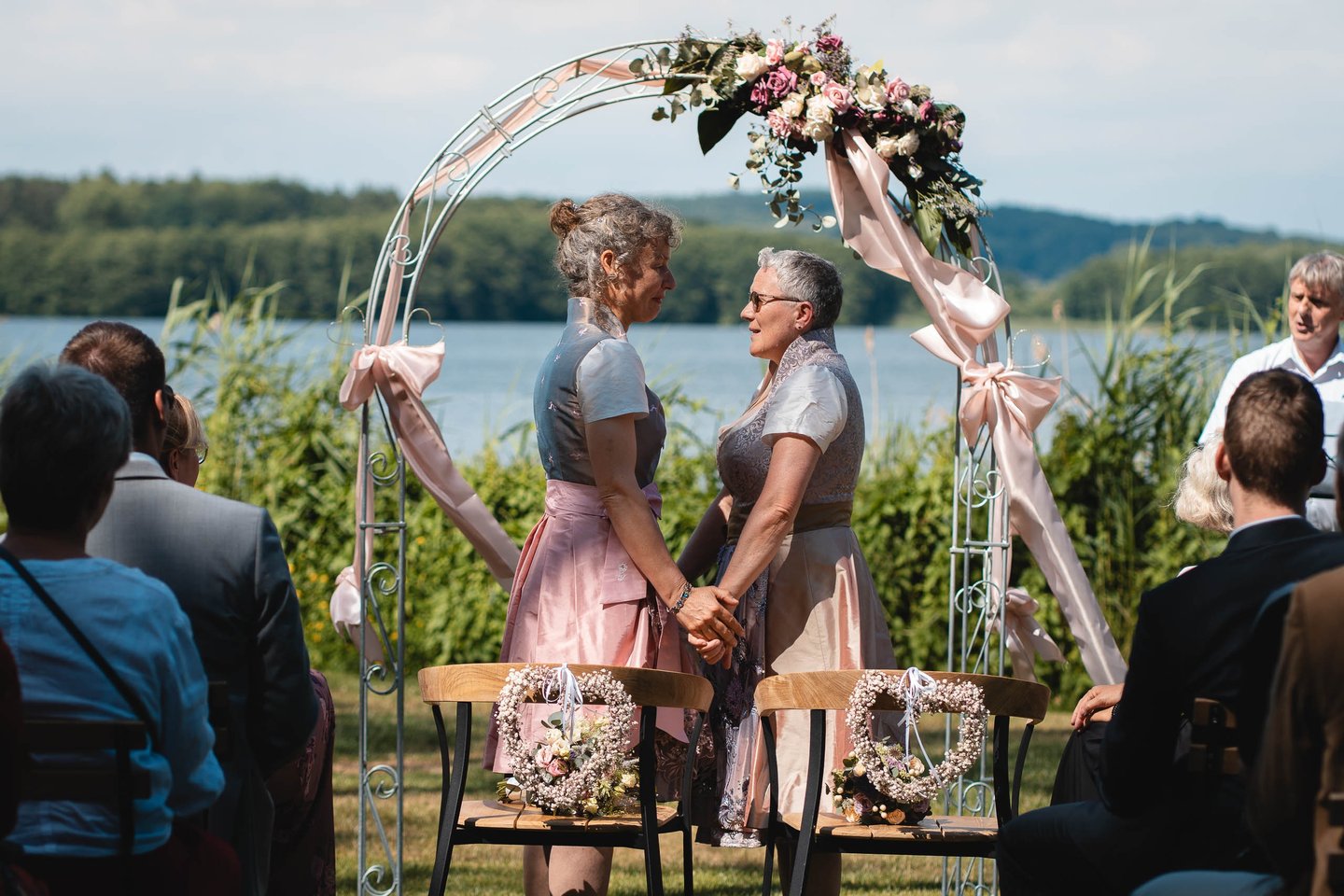 Zwei Bräute halten sich bei der freien Trauung unter einem Blumenbogen an den Händen. Foto: Joel Pingel.