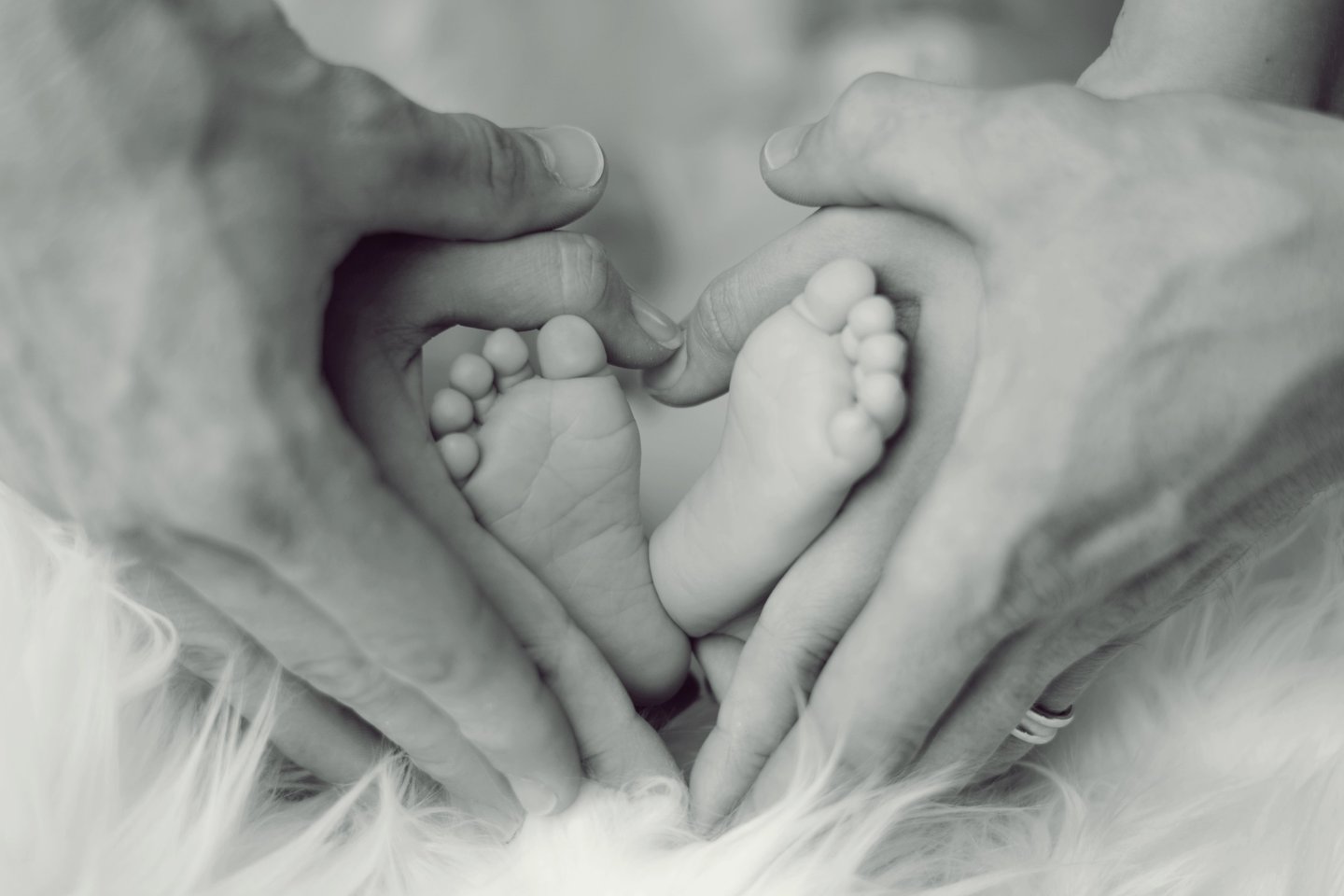 Mother and father’s hands holding a baby's feet in a heart shape, symbolizing love and protection