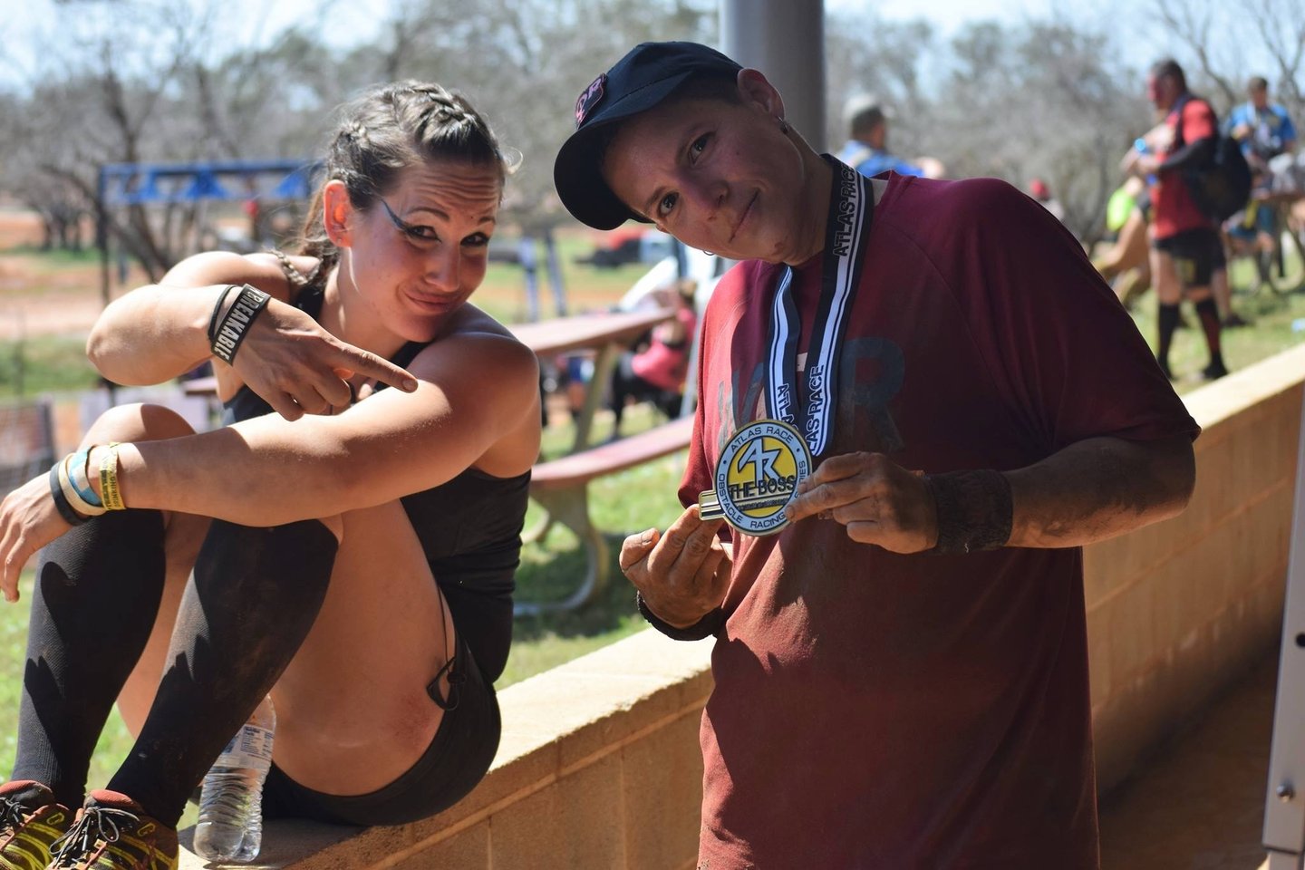 Two athletes celebrating with an Atlas Race finisher medal at an outdoor obstacle course event.