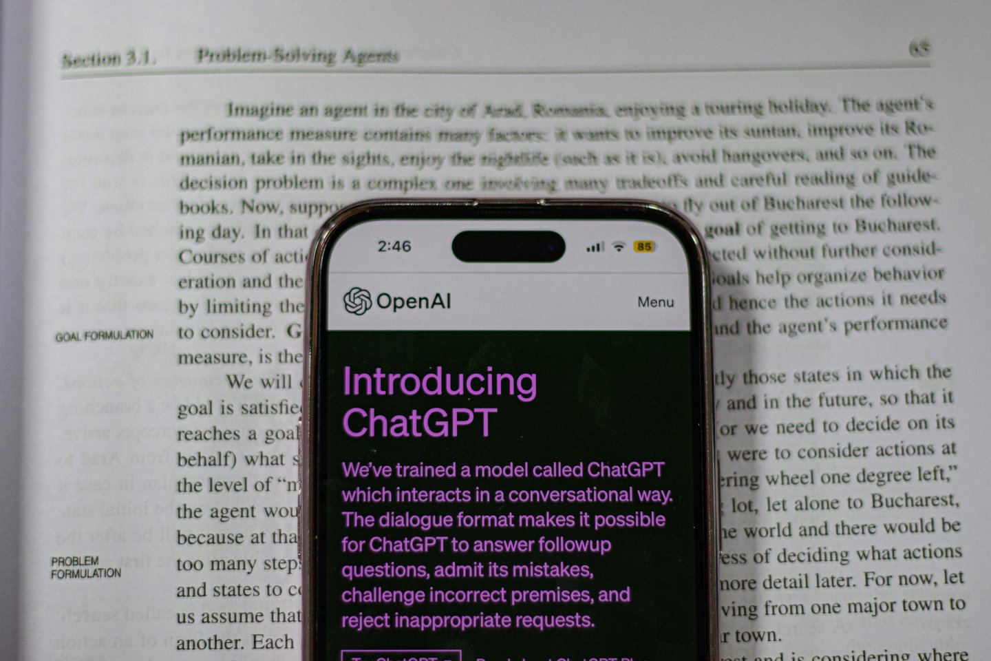 A mobile over a book, in the mobile's display an app ChatGPT is displaying.