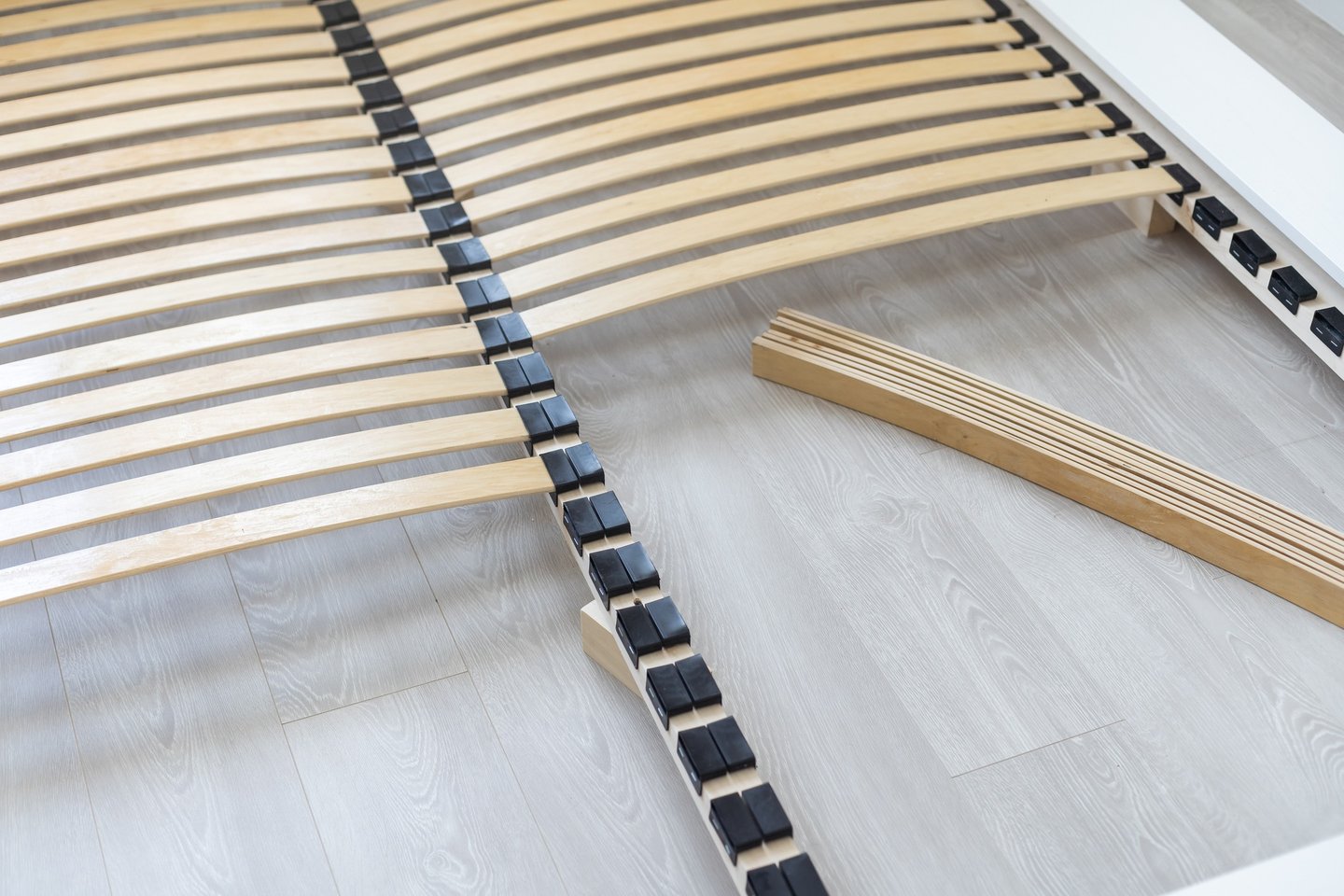 Close-up of a wooden slatted bed base frame being assembled on a light laminate floor.