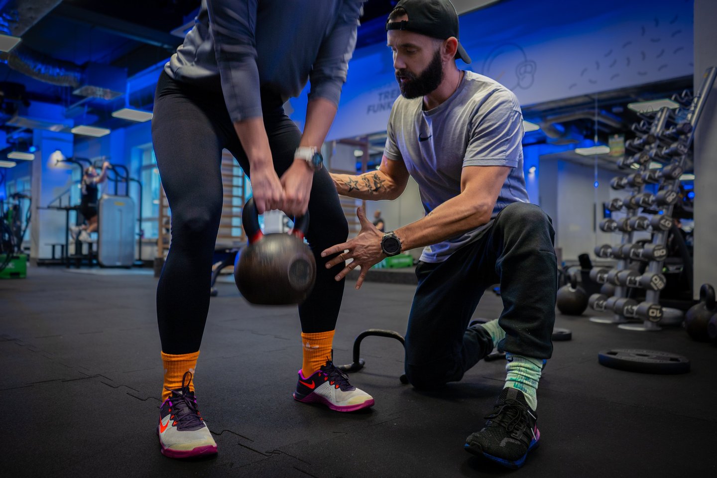 Trener instruuje kobietę przy treningu z kettlebell.