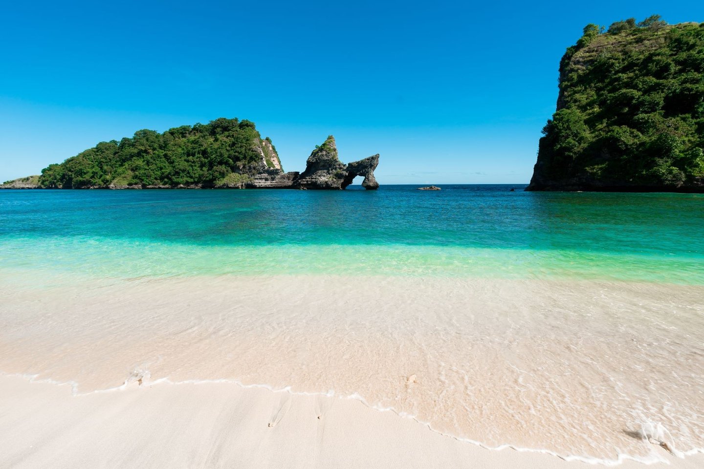 two women walking into turquoise ocean on a white sandy beach with limestone cliffs and lush green islands under blue sky