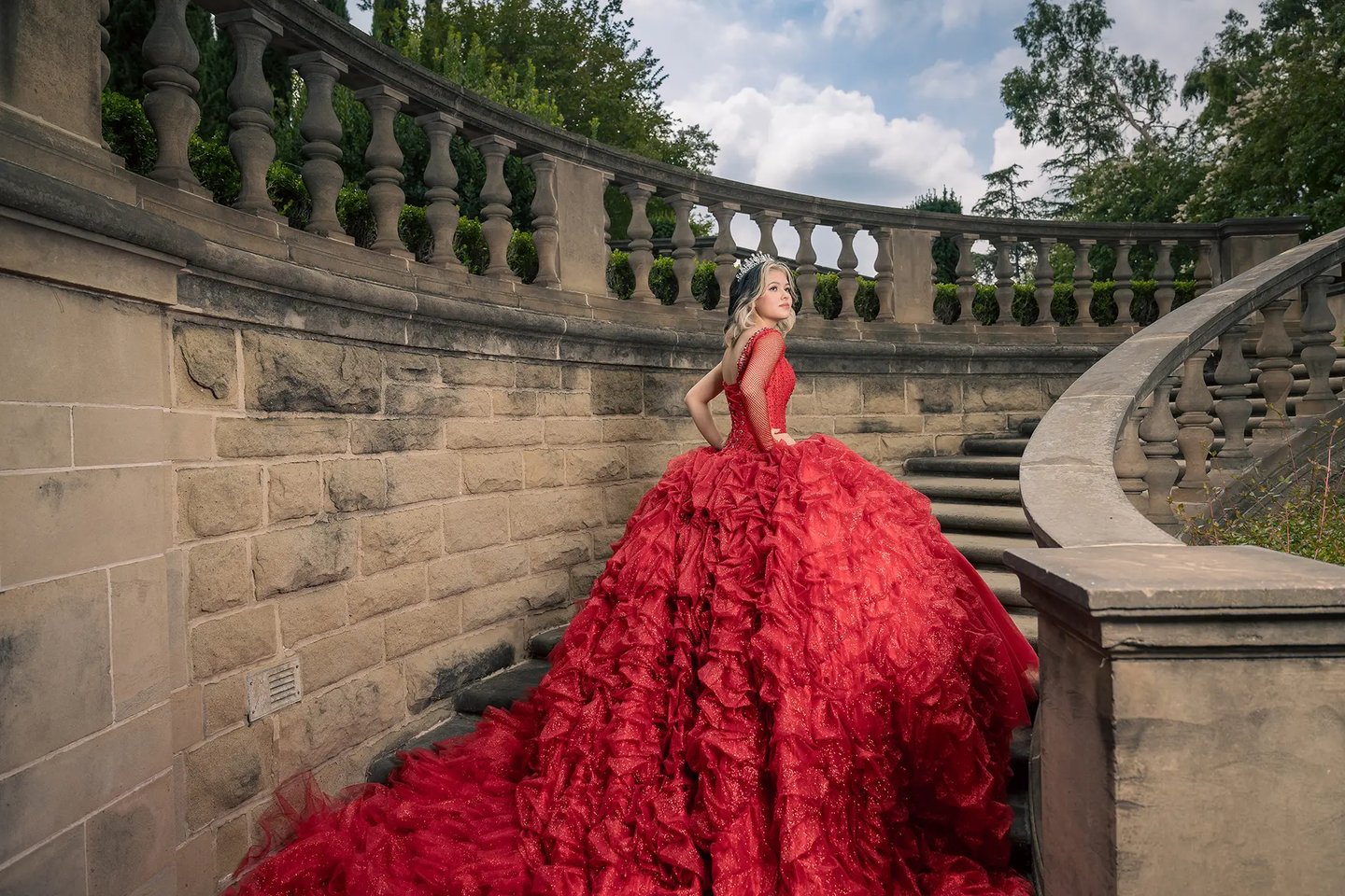 a quinceañera in a red dress standing on a staircase