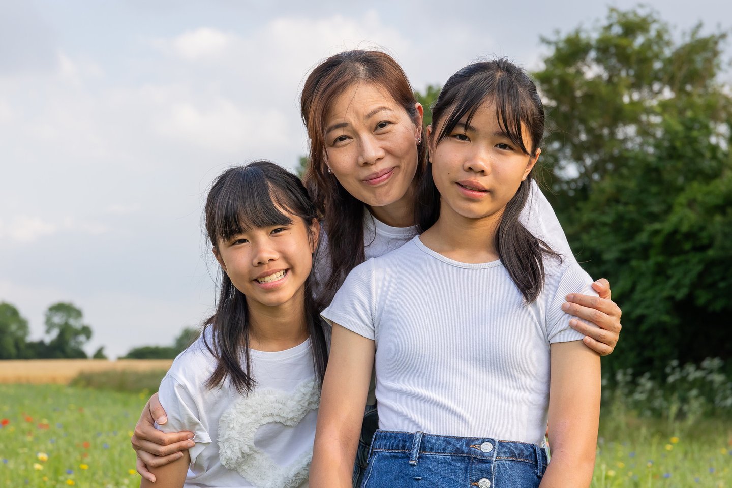 a woman and two young girls in a field smiling towards the camera