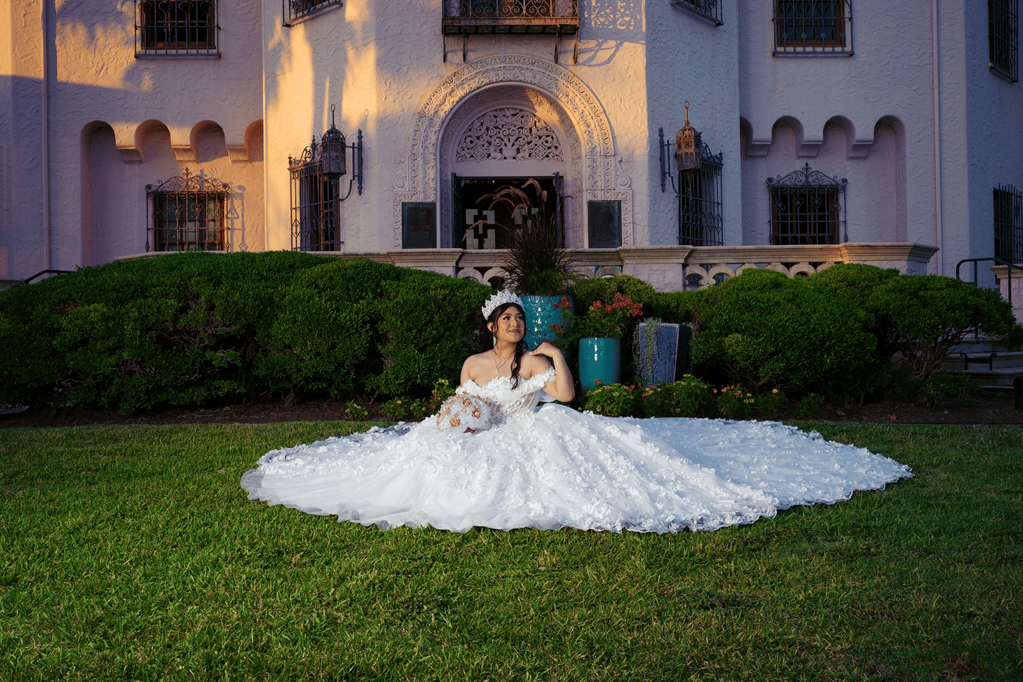 a woman in a wedding dress sitting posing for photographer on a lawn