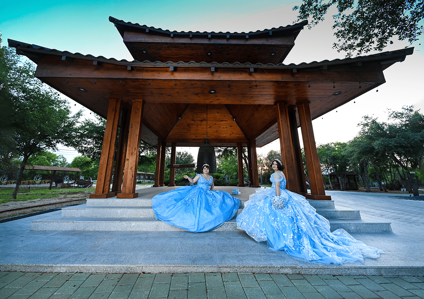 two women in blue quinceanera dresses pose for photographstanding in front of a pagoda