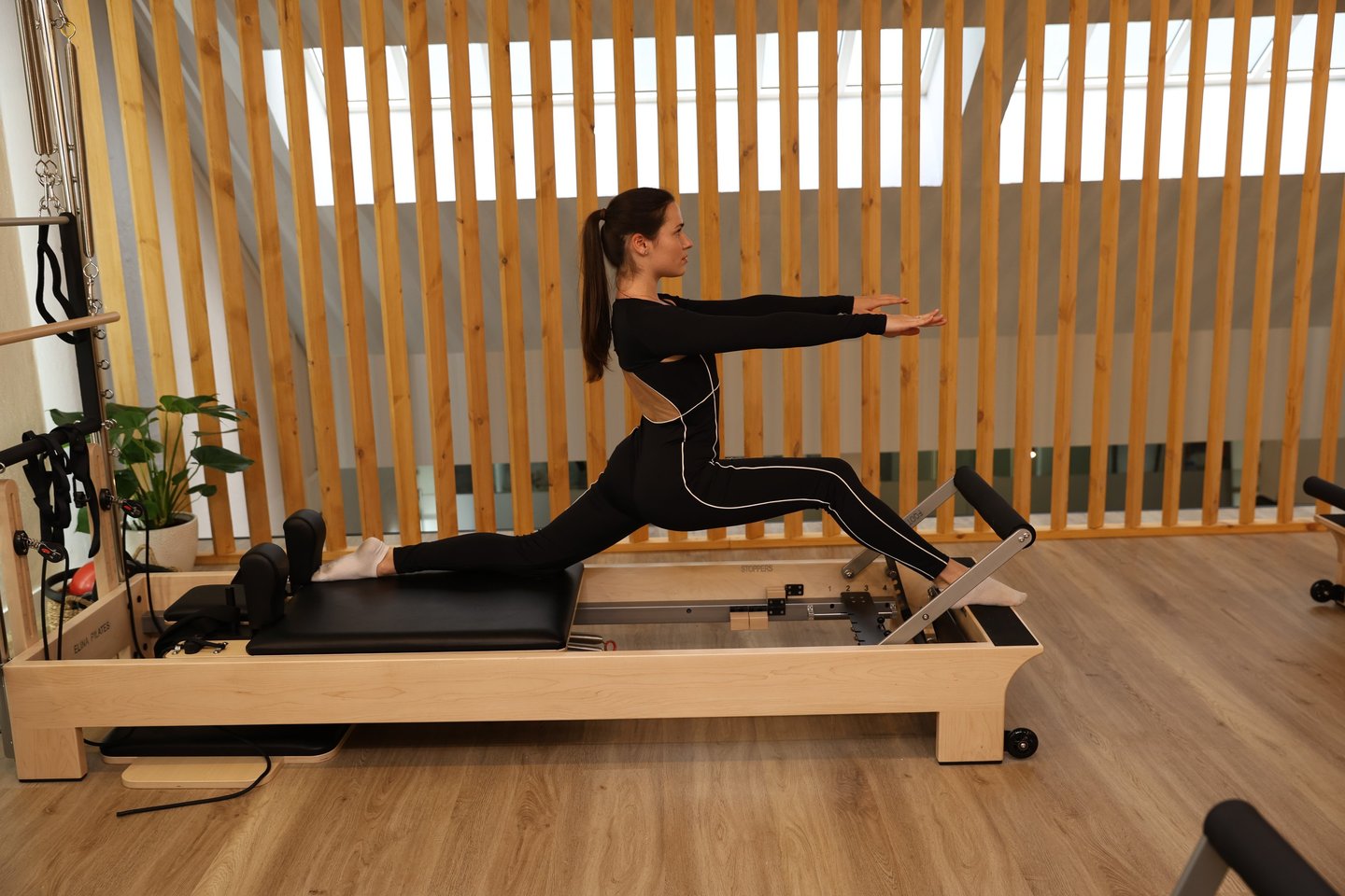 Uma mulher a realizar um alongamento em abertura no reformer num estúdio moderno 