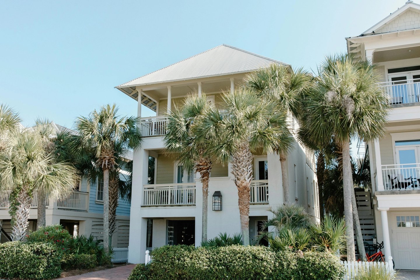 Luxury three-story beach house rental with palm trees and balconies under a clear blue sky.