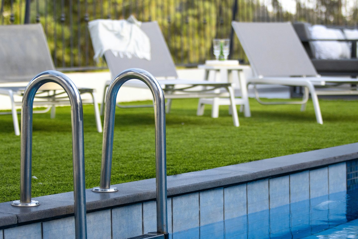 Stainless steel swimming pool ladder handrail on a luxury patio with artificial grass and lounge chairs.