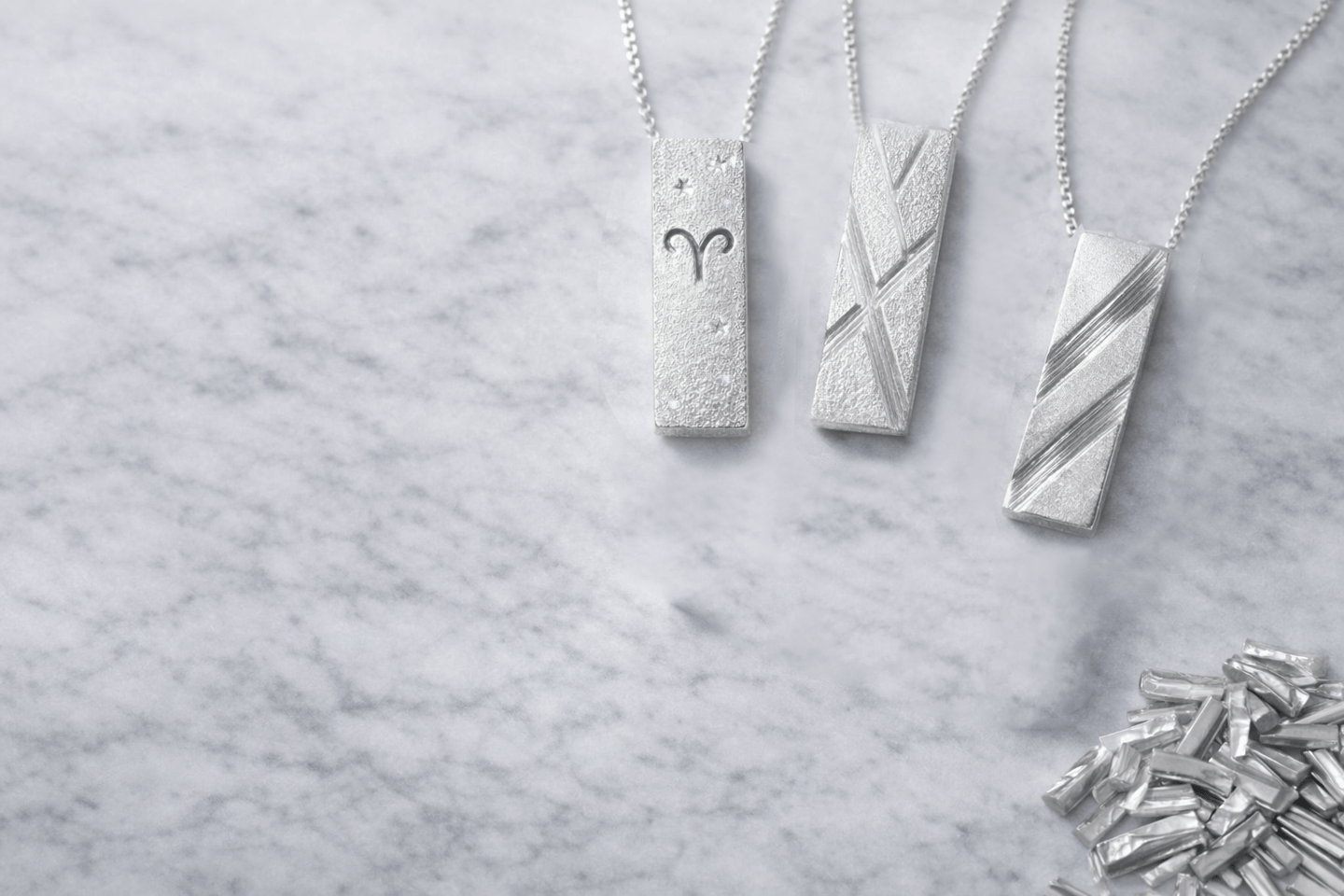 Minimalist silver pendants displayed on marble, highlighting clean lines and texture