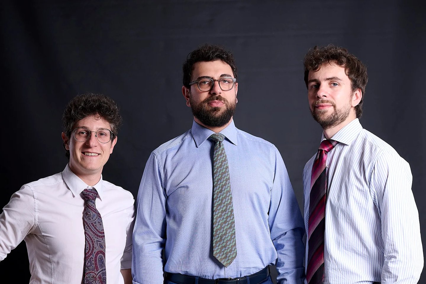 Three professional men in dress shirts and ties posing for a corporate portrait.