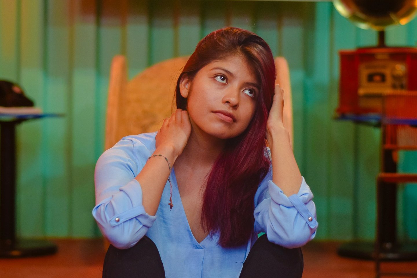 A pensive young woman with auburn hair sits in a vintage room with a gramophone.