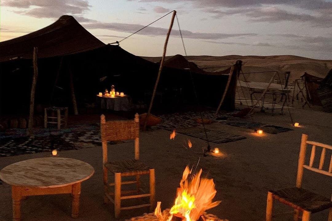 A glowing campfire at a luxury desert camp in Morocco with traditional tents and seating at dusk.