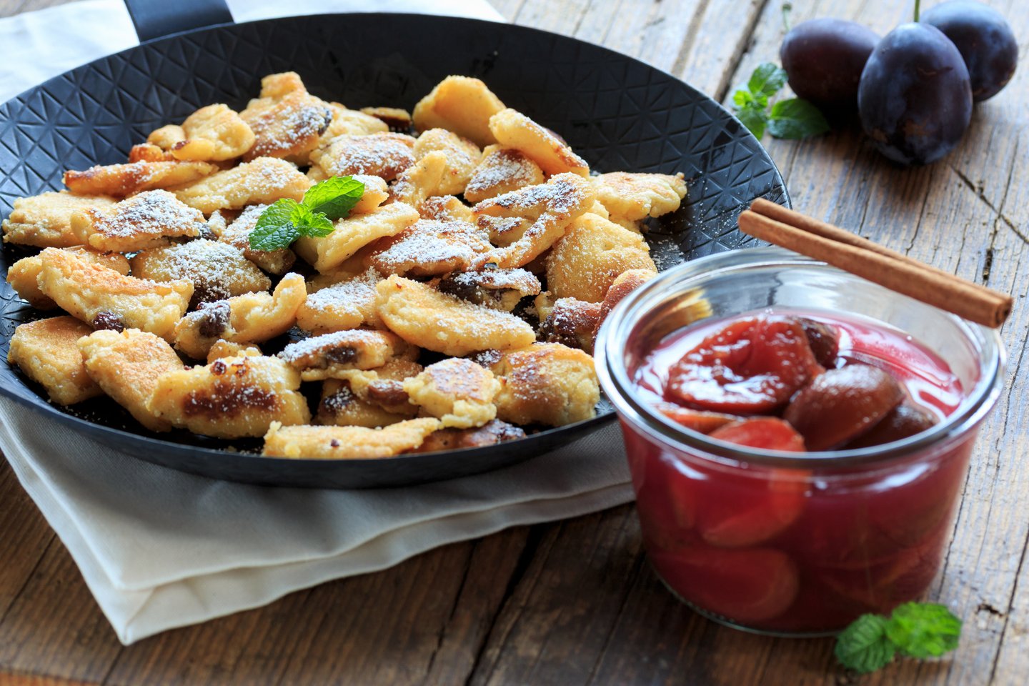 Traditional Austrian Kaiserschmarrn shredded pancake with powdered sugar and plum compote in a jar.