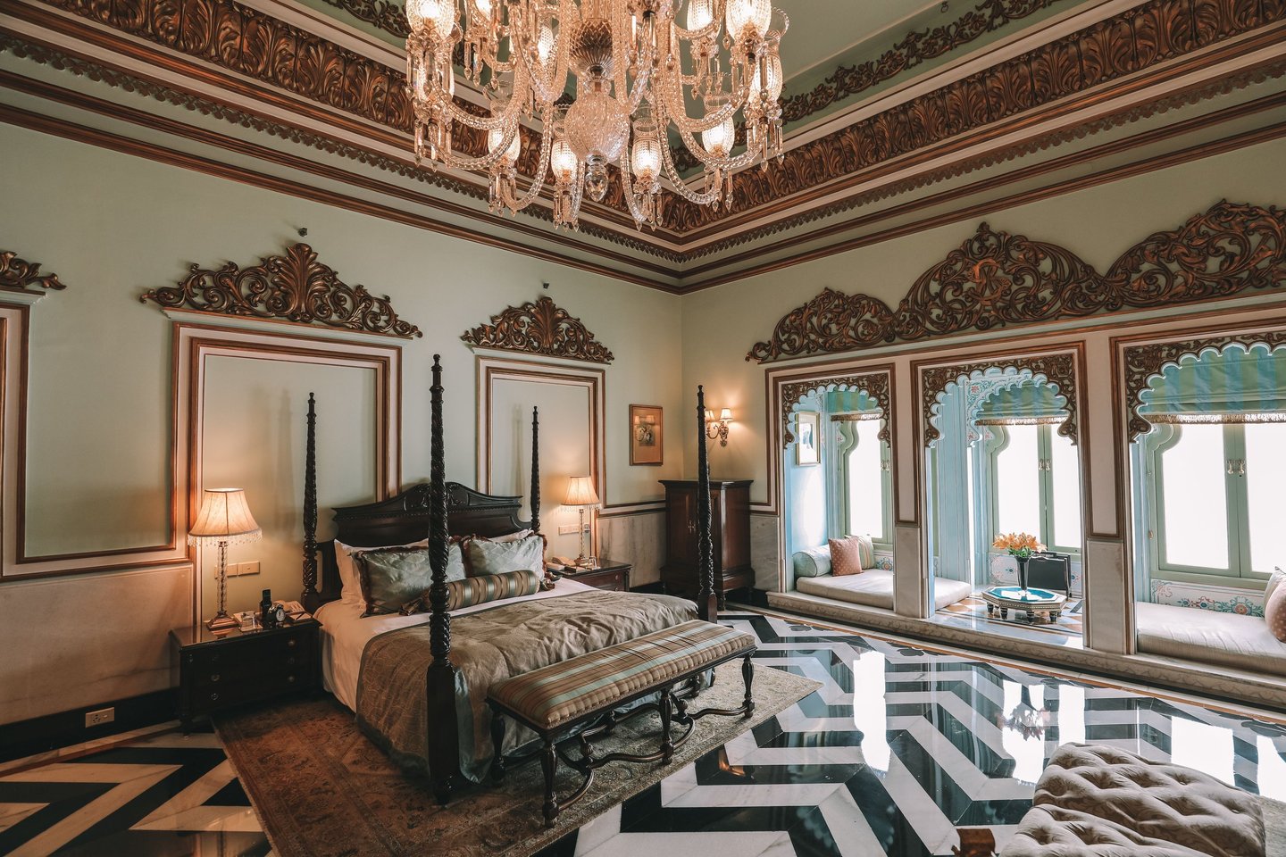 Luxury royal suite with a four-poster bed, ornate crystal chandelier, and marble chevron floors in an Indian palace.