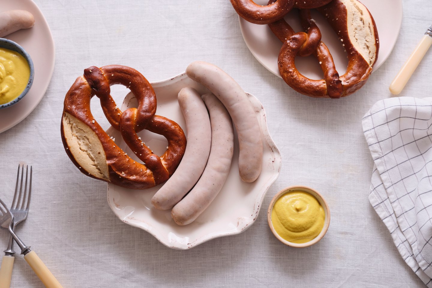 Traditional German breakfast with Weisswurst white sausages, soft pretzels, and sweet mustard on a table.