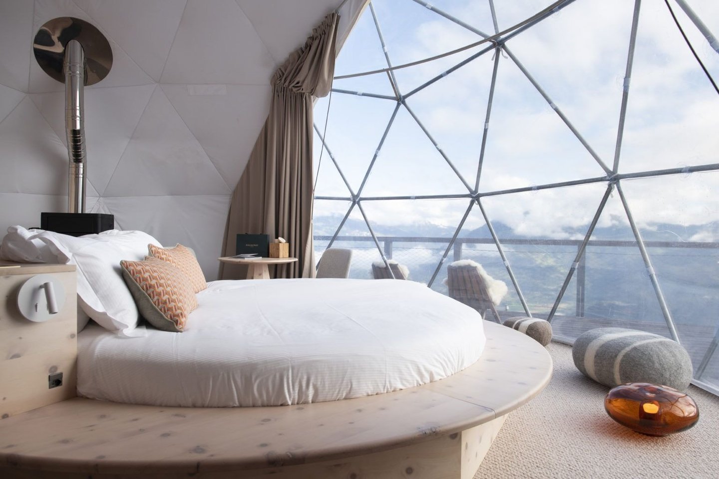 Luxury geodesic dome interior featuring a round bed and scenic mountain views through glass panels.