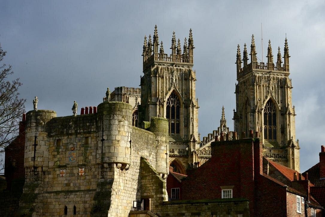 The historic stone towers of York Minster cathedral rise behind a medieval city wall under a grey sky.