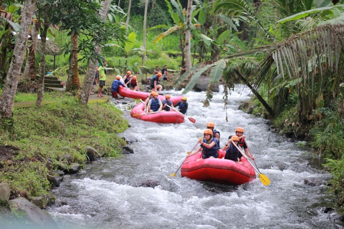 Tourists enjoy white water rafting in red boats down a tropical river in Bali.
