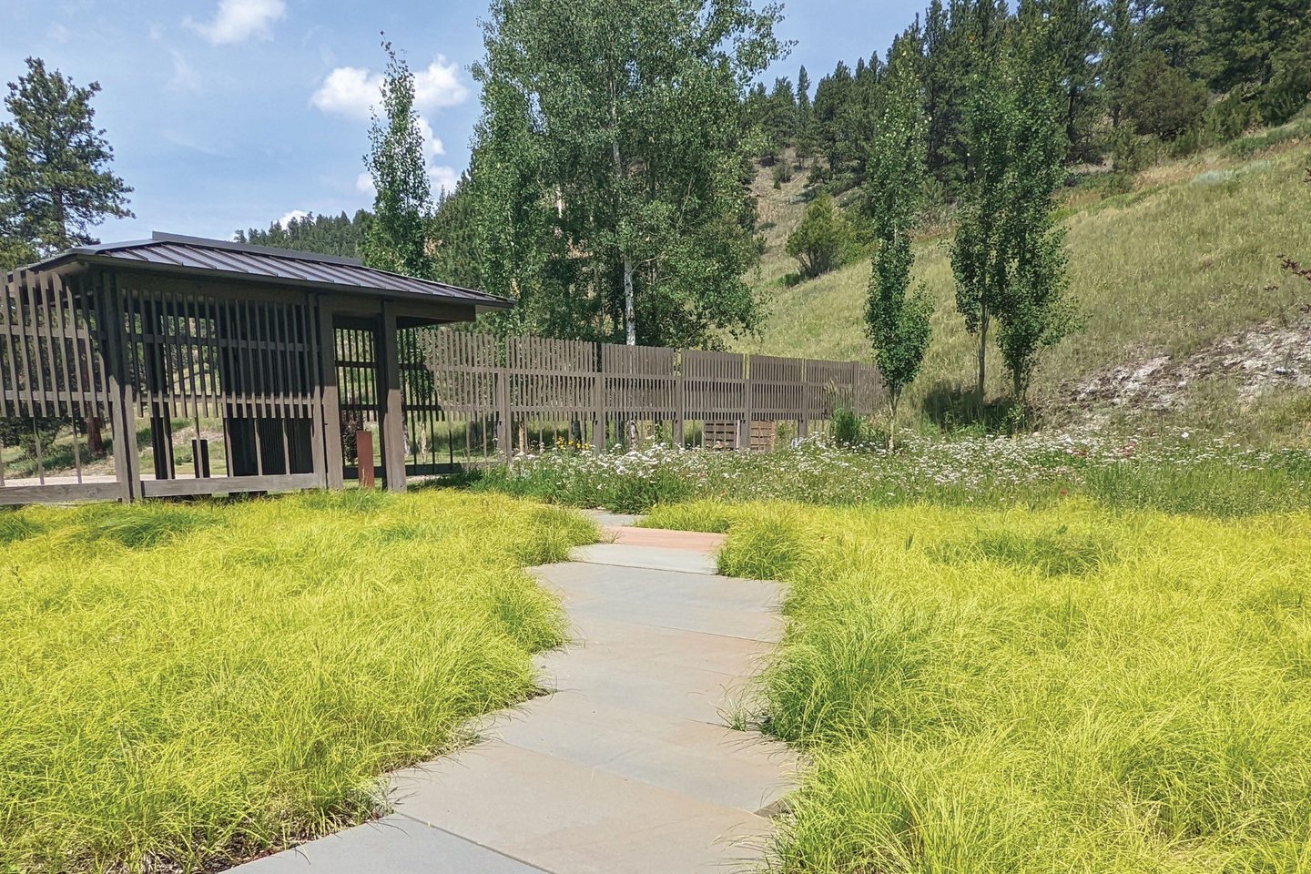 a stone pathway through a sedge lawn and wooden gate housee