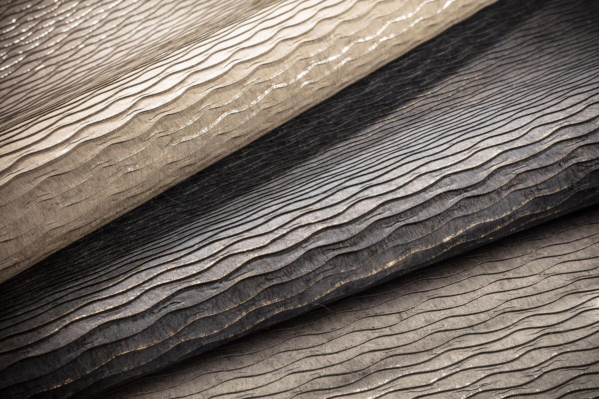 Textured luxury wallpaper samples with elegant metallic wavy patterns in beige, charcoal, and bronze tones.