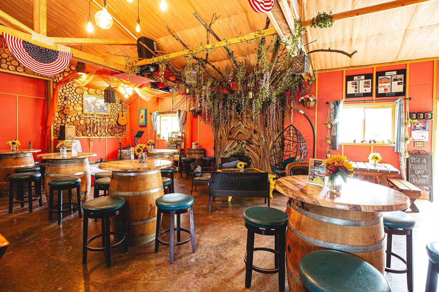 Rustic winery tasting room featuring wine barrel tables, teal bar stools, and floral decor.