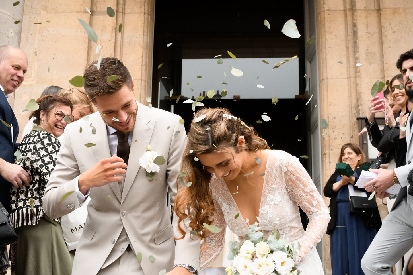 La mariée et le marié sous un jeté de pétales et de fleurs, à la sortie de l'église