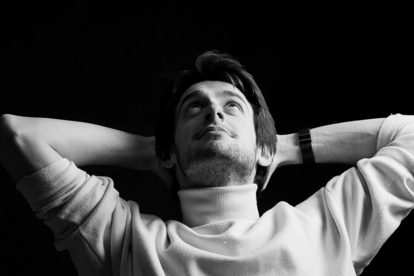 Un jeune homme décontracté les bras derrière les tête en photo noir et blanc de studio