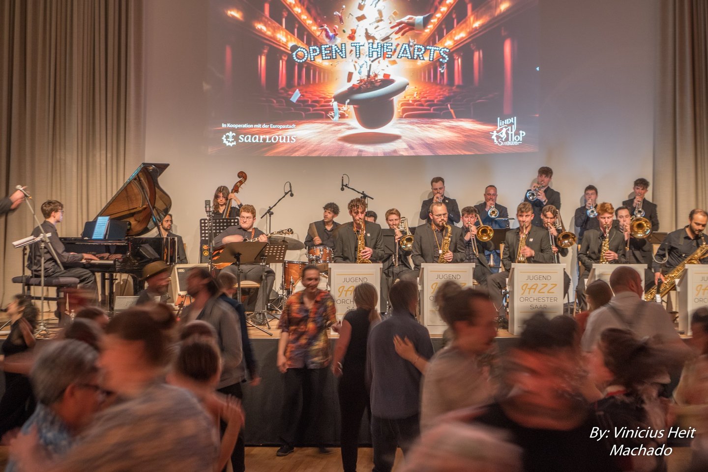 A live big band jazz orchestra performing on stage while people dance at a swing dance event.