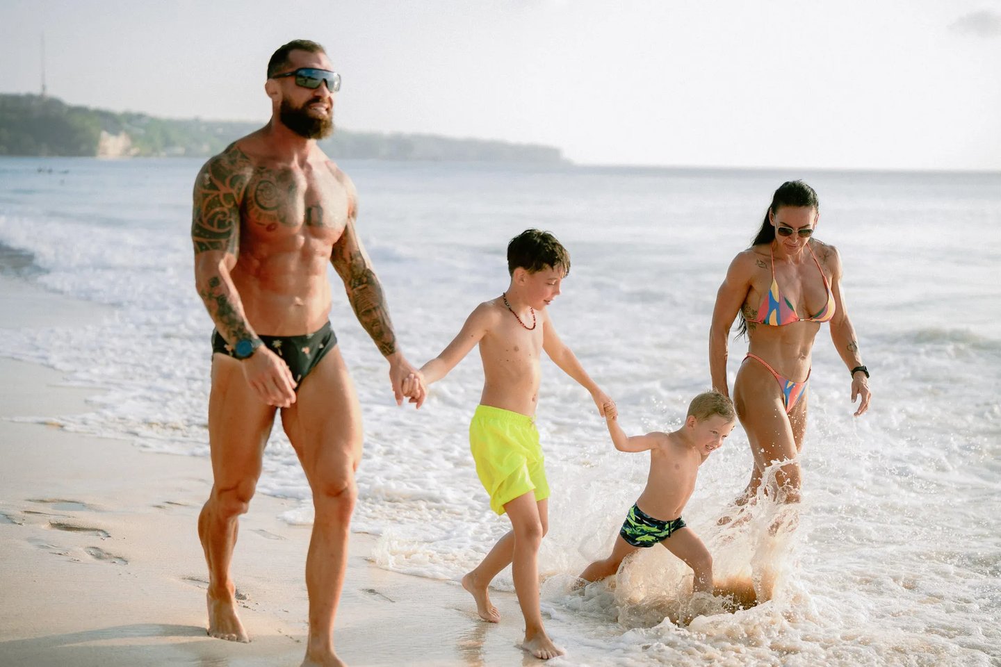 Family enjoying playful moments together near the ocean during a candid family photography session at Dreamland Beach Bali.