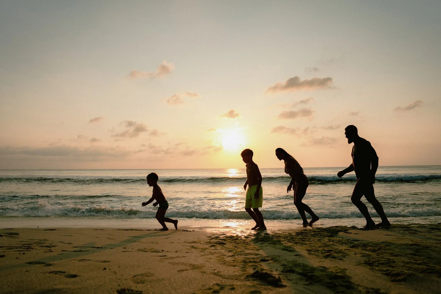Parents and child running together along the shoreline during golden hour at Dreamland Beach Bali.