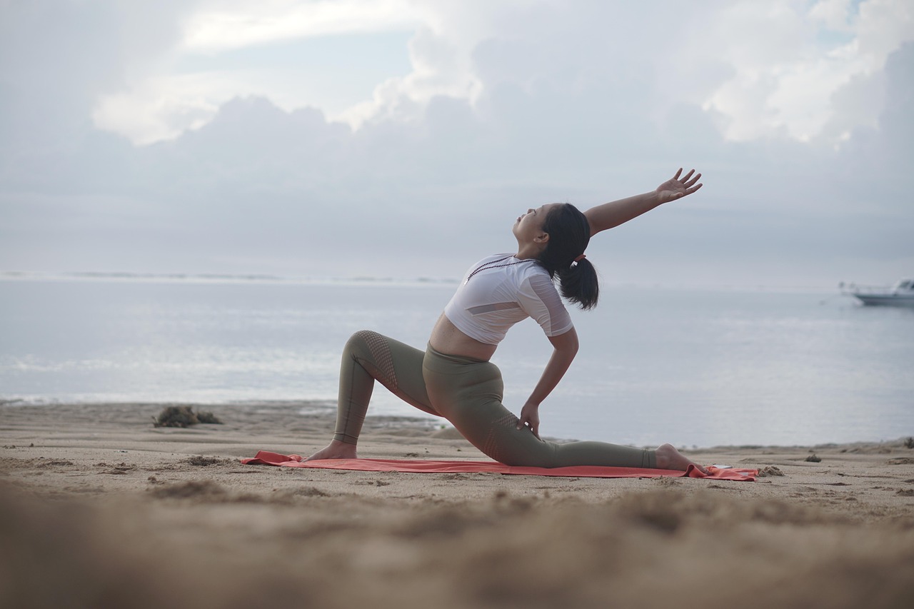 Woman stretching on a beach at sunrise, practicing active recovery with yoga to promote muscle flex